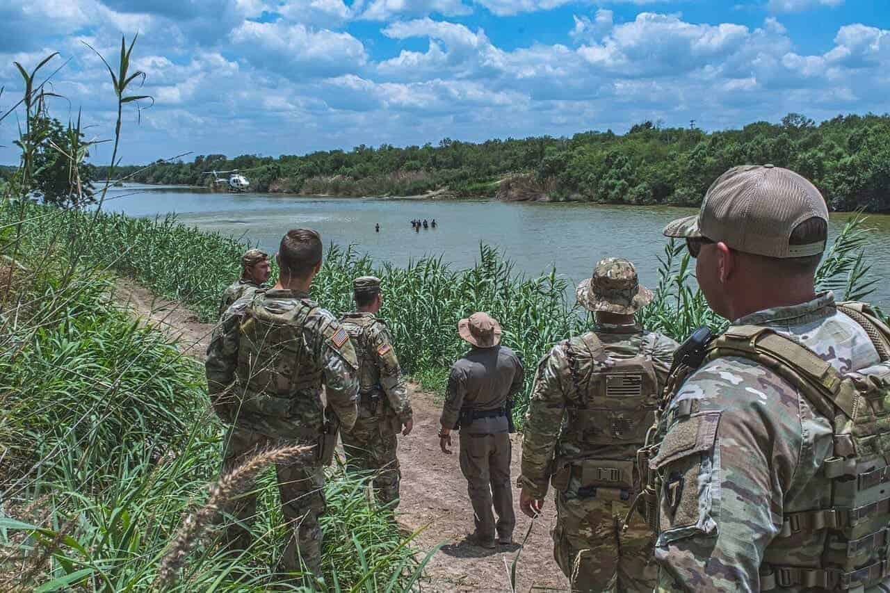 Members of the Texas National Guard watch a Border Patrol helicopter hover above a group of civilians wading in the Rio Grande along the Texas-Mexico border during Operation Lone Star.