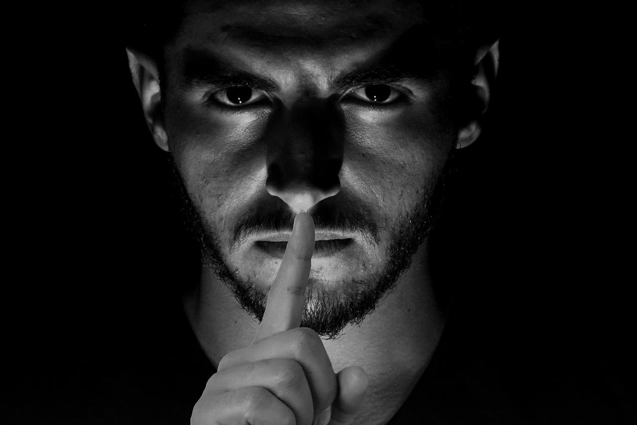 censorship shhh Thought police dark photo of man with finger to his lips symbolizing censorship by microsoft