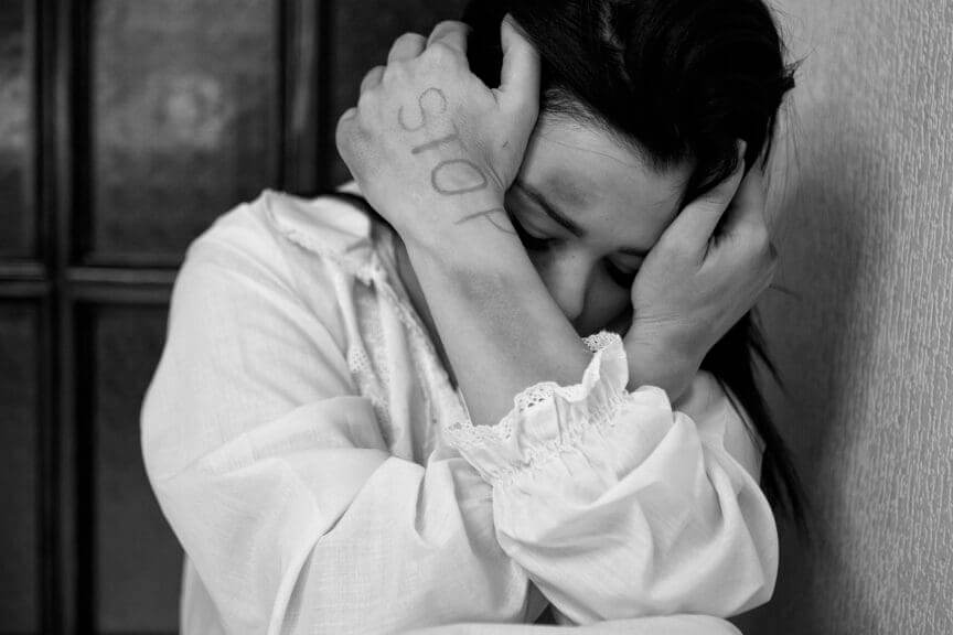 Victim of domestic violence. A woman crouched down, shielding her face with bruises on her arm.