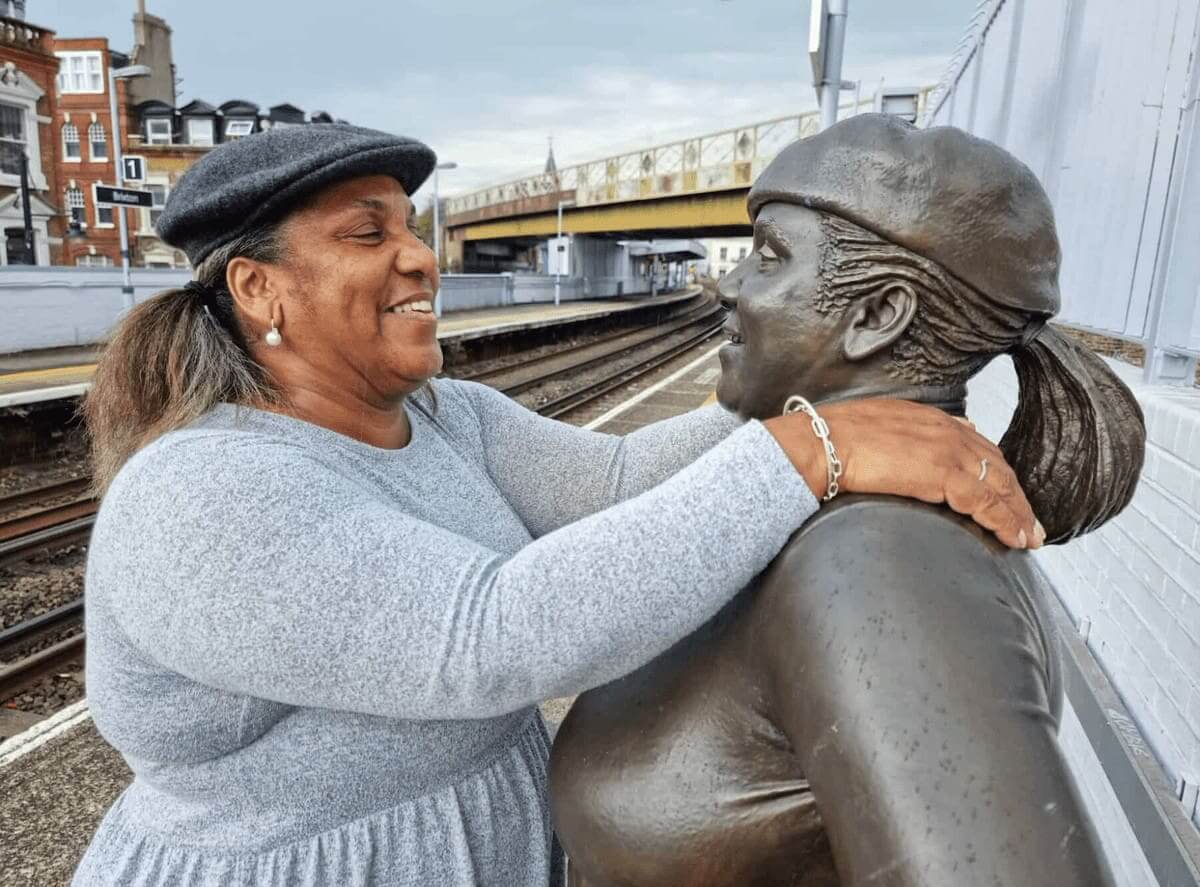 Woman with her arms over the shoulders of a statue of women