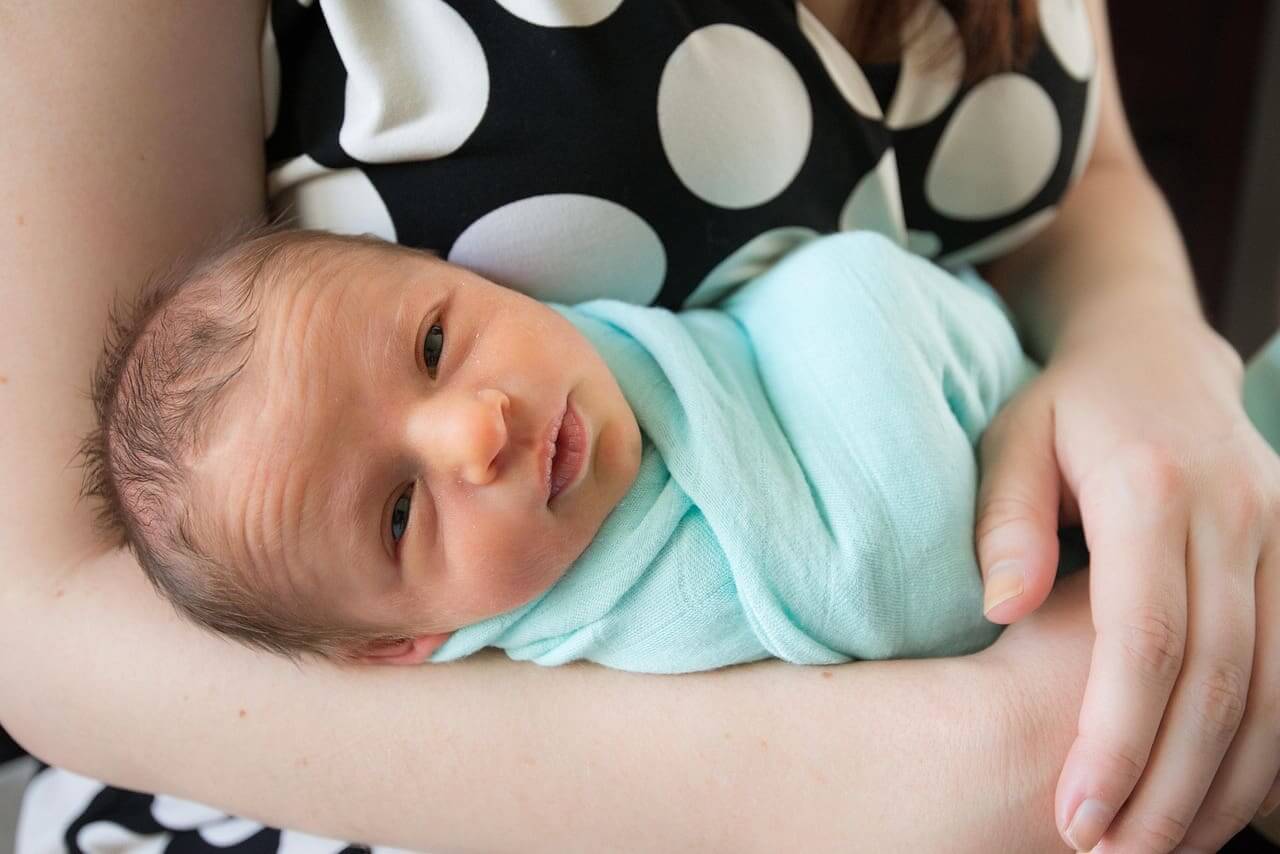 Newborn baby in someone’s arms looking at the camera.