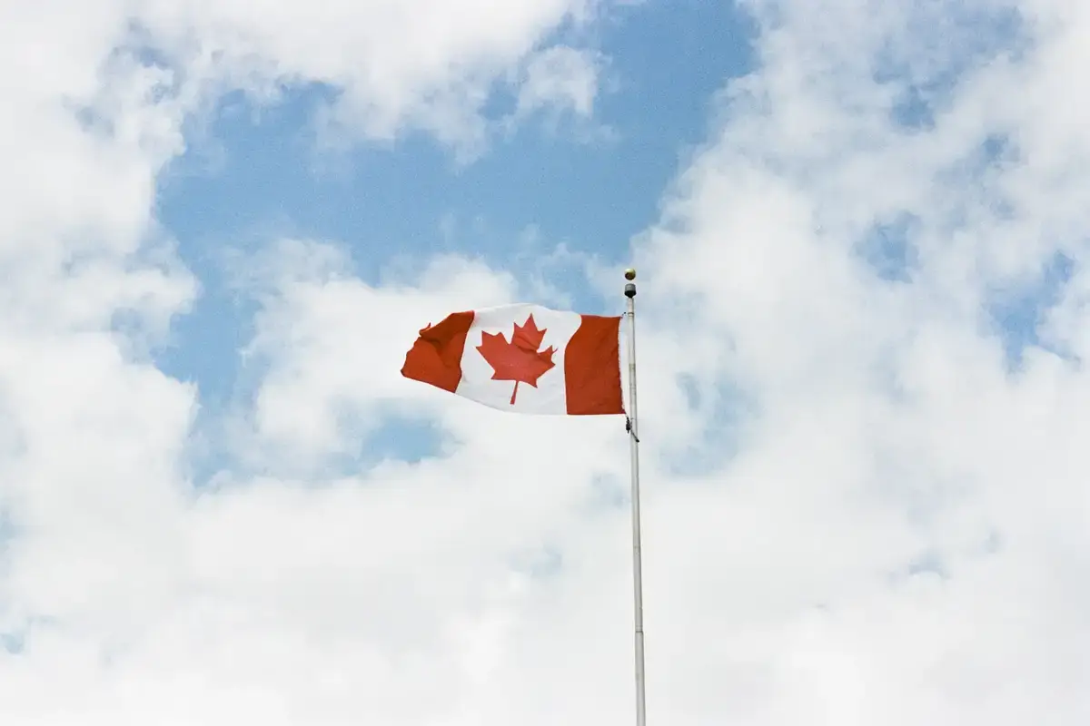 canadian flag against cloudy sky Canadian flag against a cloudy blue sky