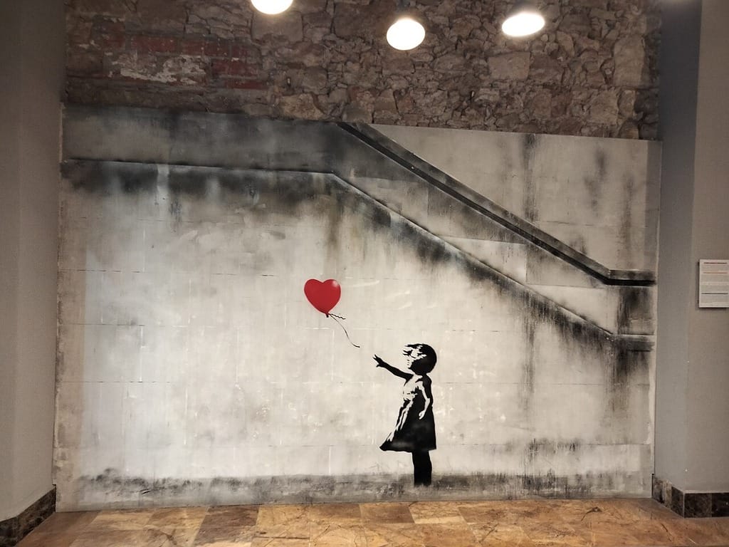 banksy art girl red balloon A graffiti art design by banksy of the little girl holding a red heart balloon.