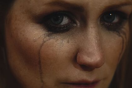Close-up of a woman with smeared makeup and tears on her face showing deep emotion.