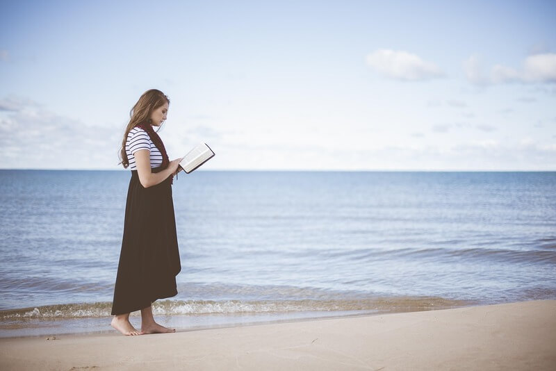woman holding a bible Woman walking on the beach reading a bible